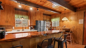 Una cocina de madera con una isla grande, taburetes de bar y un refrigerador.