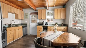 Une cuisine avec des meubles de rangement en bois, une table à manger avec des chaises et une fenêtre avec des stores.
