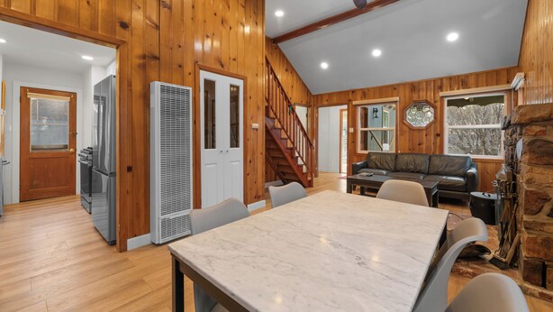 A spacious room with a marble table, wooden walls, a staircase, and a stone fireplace. - Big Bear Cottage - Walk to Lake, Apple TV, Fireplace, Deck (Big Bear Lake)