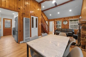 A spacious room with a marble table, wooden walls, a staircase, and a stone fireplace.