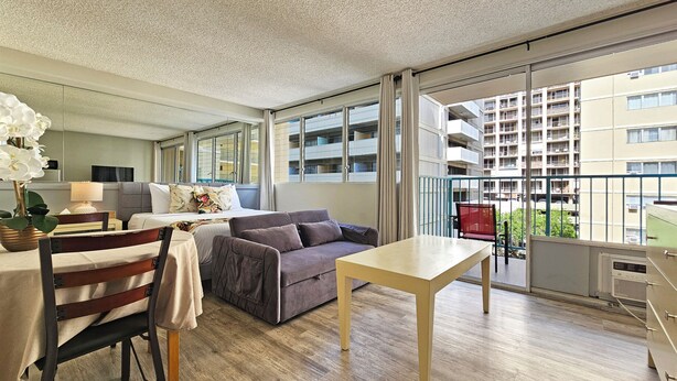 A modern living room with a sofa, a dining table, and a balcony with a view of a residential building.