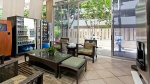 A modern indoor seating area with a glass-top table, wicker chairs, and a vending machine.