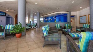 A lobby with wicker furniture, potted plants, and a reception area with a blue wall and a clock.
