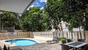 A pool area with stone flooring, a table with chairs, and a fenced area with trees.