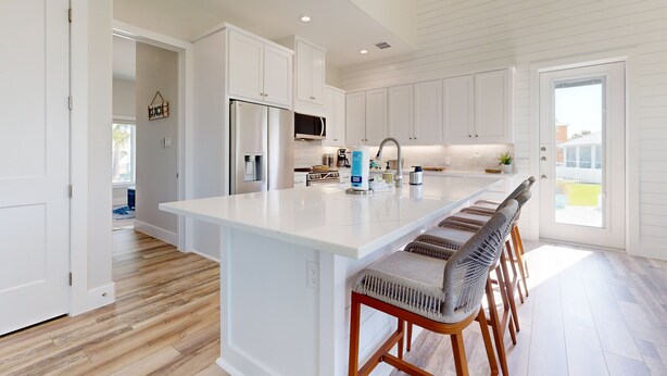 Una cocina moderna con armarios blancos, una isla grande con taburetes y vistas al exterior.