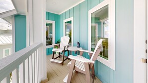 Un porche cubierto con paredes azul turquesa y detalles blancos, con dos sillas Adirondack y una pequeña mesa.