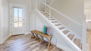 Una escalera con barandillas blancas y peldaños de madera, un banco con cojines y una puerta que da al exterior.