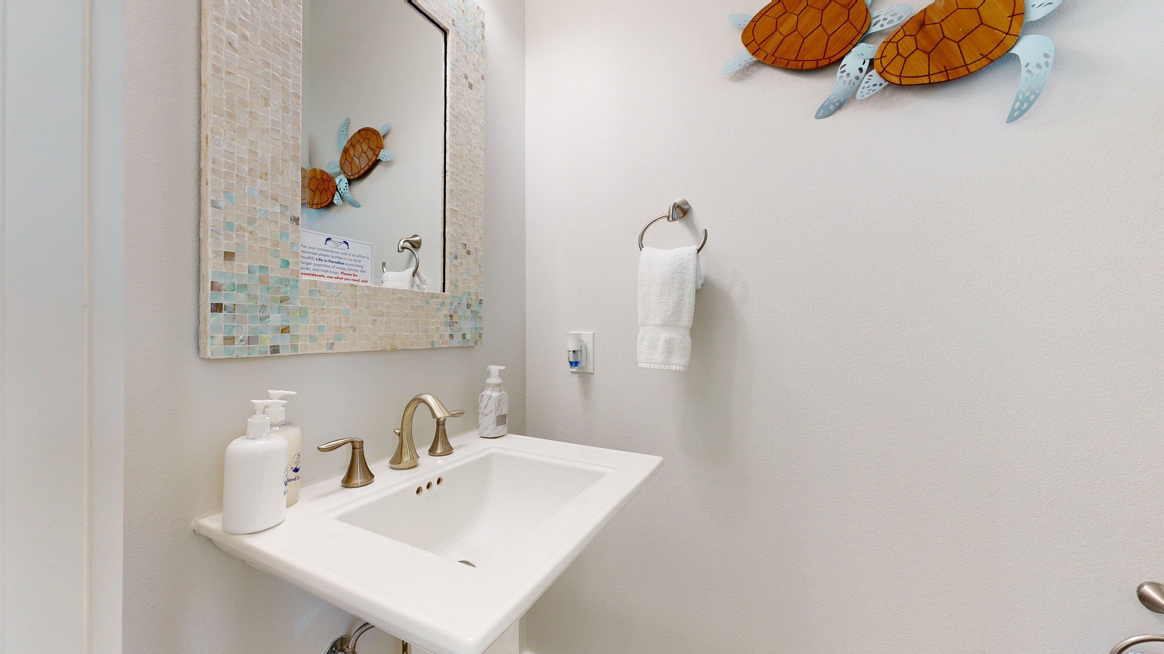 A bathroom with a white sink, two faucets, a mirror with a mosaic backsplash, a soap dispenser, and a towel rack.