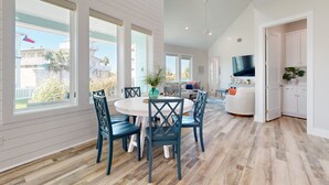 Una sala de estar amplia con un televisor grande, una zona de comedor con una mesa redonda y sillas, y una cocina con alacenas y encimera.