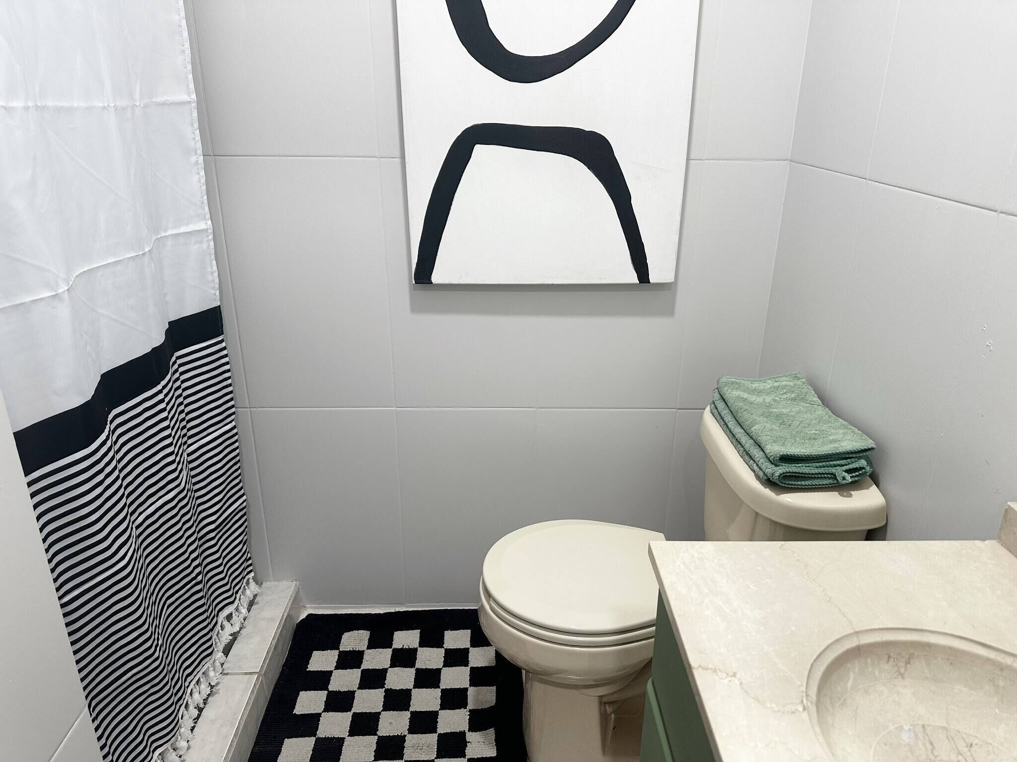 Kylpyhuoneessa on ruutukuviollinen lattia, wc-istuin, pesuallas ja pyyhe seinällä.