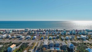 Vue aérienne d’une zone résidentielle côtière, avec des maisons, une plage et un ciel dégagé.