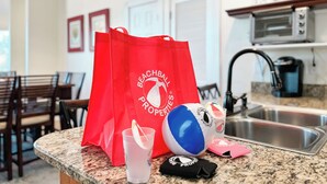 Un comptoir de cuisine avec un sac rouge, un ballon de plage bleu et blanc, un gobelet en plastique et un objet noir orné d’un logo.