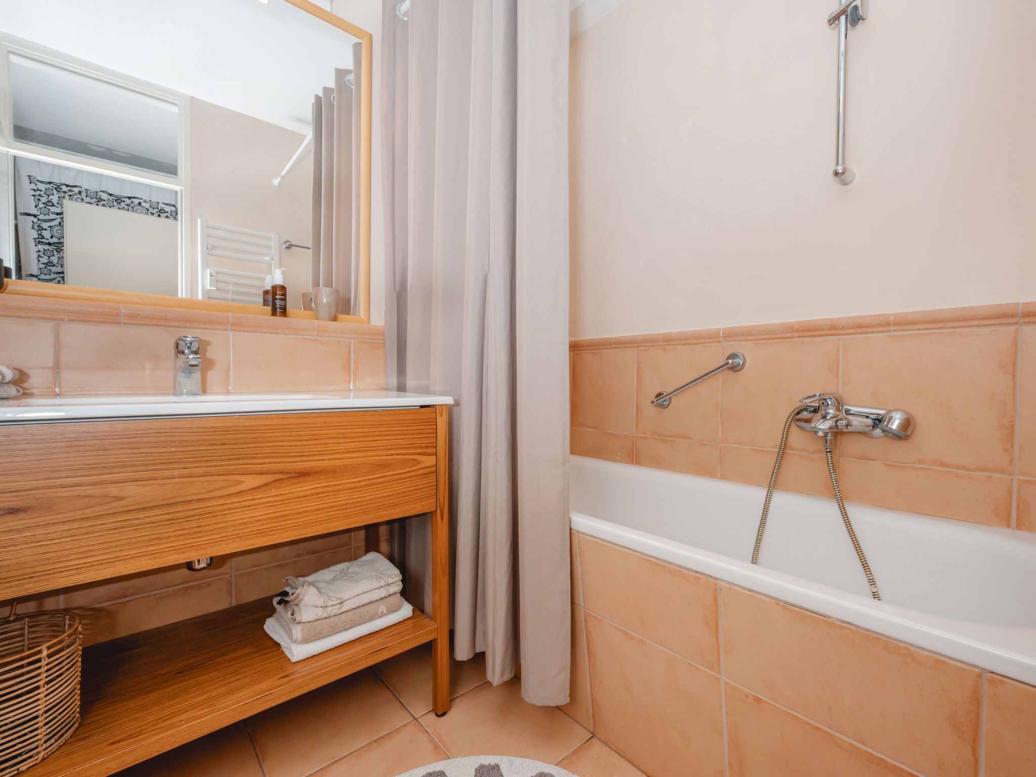 A bathroom with a wooden vanity, a mirror, a shower with a handheld showerhead, and a towel rack.