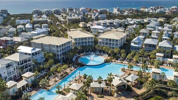 Un resort con una piscina central, varias villas para huéspedes y vista al océano.