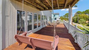Una terraza cubierta de madera con un columpio y un banco, con vista a una zona residencial con una casa y palmeras.