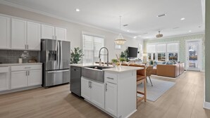 A modern kitchen with white cabinets, stainless steel appliances, and a central island. - Chic Coastal Retreat  Water Views • Pool • Fire Pit • Steps to Beach (Orange Beach)