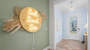 A hallway with a neon sign reading "Salt, Sand, Sea" on the wall, a patterned rug, and a door with a window. - Chic Coastal Retreat  Water Views • Pool • Fire Pit • Steps to Beach (Orange Beach)