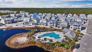 A residential area with multiple houses, a large swimming pool, and a body of water. - Chic Coastal Retreat  Water Views • Pool • Fire Pit • Steps to Beach (Orange Beach)