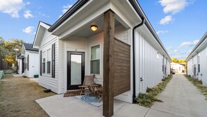 Un conjunto de casas de un piso con porche cubierto, un sendero de concreto y un pequeño patio con mobiliario exterior.