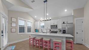 Una cocina moderna con armarios blancos, un refrigerador de acero inoxidable, un microondas y una isla grande con taburetes rosados.