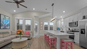 Una cocina moderna con armarios blancos, un refrigerador de acero inoxidable y una isla central con taburetes rosados.