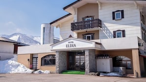 A hotel named 'Eldia' with a stone facade, a balcony, and a mountain backdrop. - Hotel Eldia Madarao (Myoko)