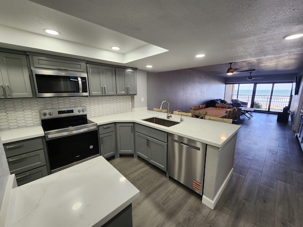 A modern kitchen with a large island, stainless steel appliances, and a view to a balcony with outdoor seating.
