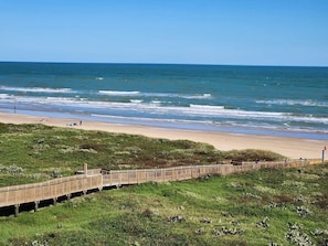 A beach with a wooden boardwalk leading to the shore, grassy dunes, and the ocean.