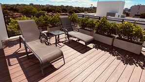 Eine Dachterrasse mit Holzboden, zwei Liegestühlen, einem kleinen Tisch und Kübelpflanzen.