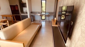 Ein modernes Wohnzimmer mit einer Couch, einem an der Wand montierten Fernseher und einer Küche im Hintergrund.