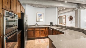 A modern kitchen with wooden cabinets, stainless steel appliances, a marble countertop, and a built-in oven.