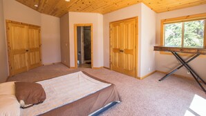 A bedroom with a wooden ceiling, a bed with a brown blanket, a desk with a chair, and a window with a view of trees. - Charming 4-bedroom house in marvelous Truckee with WiFi, fitness room (Truckee)