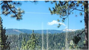 A view through a window with a wooden frame, overlooking a dense forest and a mountain range with snow-capped peaks. - Charming 4-bedroom house in marvelous Truckee with WiFi, fitness room (Truckee)