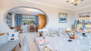 A dining area with a round table set for six, a wooden dining table, and a window with curtains. - Ty Gwyn, Holiday Cottage Manorbier, Sleeps 8, 4 bedrooms,  bathrooms (Tenby)