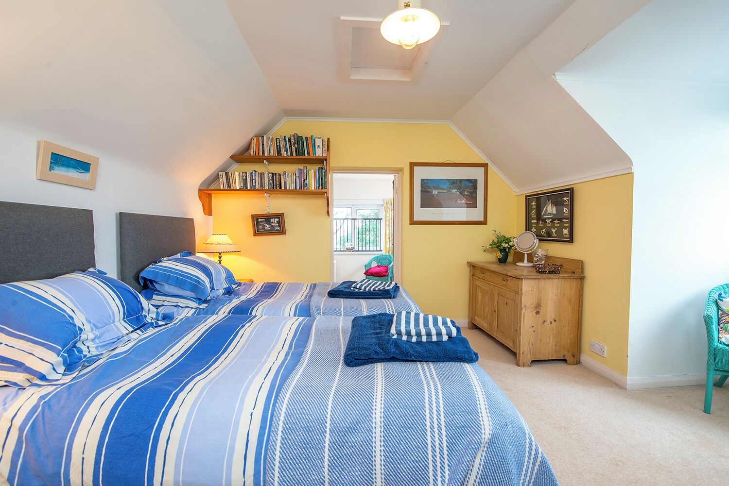 Una camera da letto con soffitto a falde, un letto con lenzuola a righe, un comò di legno e una libreria.
