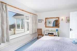 A bedroom with a large window, a wooden chair, a dresser, and a bed with a patterned bedspread. - Ty Gwyn, Holiday Cottage Manorbier, Sleeps 8, 4 bedrooms,  bathrooms (Tenby)