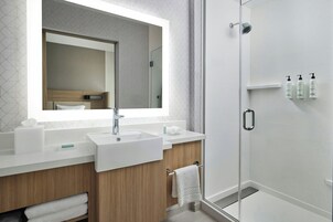 Un baño moderno con un espejo grande, dos lavamanos, una ducha y artículos de aseo en la pared.