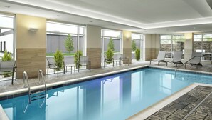A modern indoor swimming pool with clear glass walls, sunlit seating area, and a stone-tiled deck. - Springhill Suites By Marriott Troy Dayton (Troy)