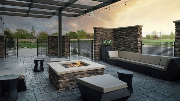 An outdoor patio with stone walls, a fire pit, and seating areas. - Springhill Suites By Marriott Troy Dayton (Troy)
