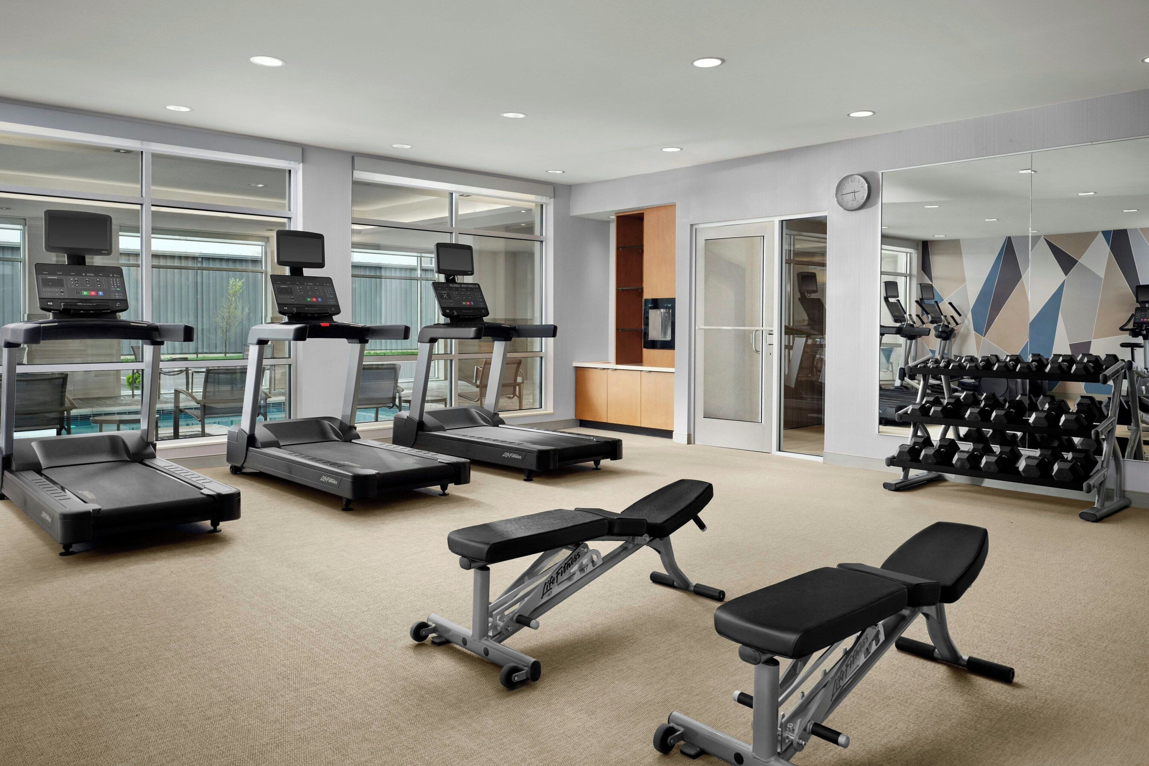 Un gimnasio con cintas de correr, una prensa de banca y un estante con mancuernas.