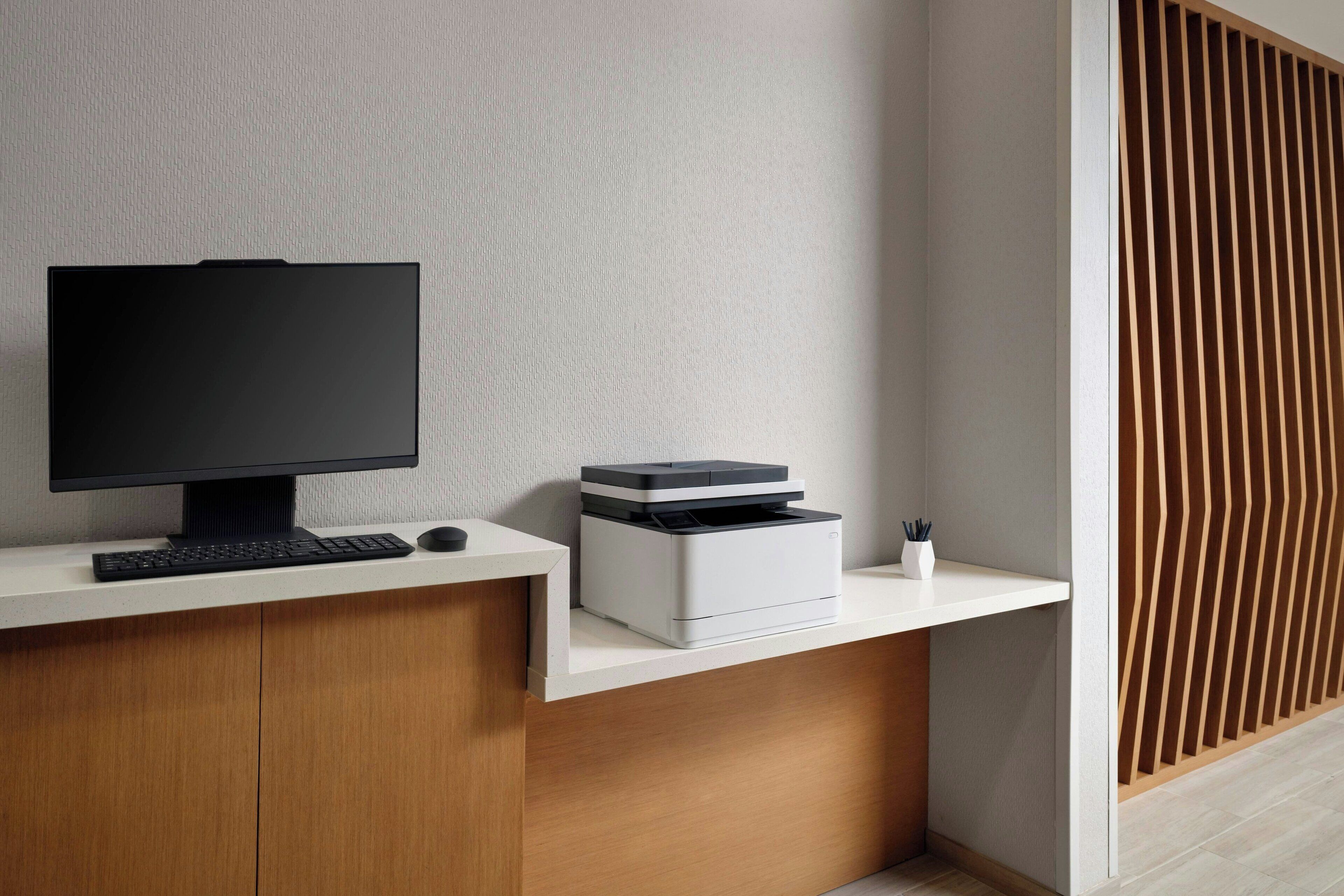 A modern desk with a flat-screen monitor, keyboard, and printer.