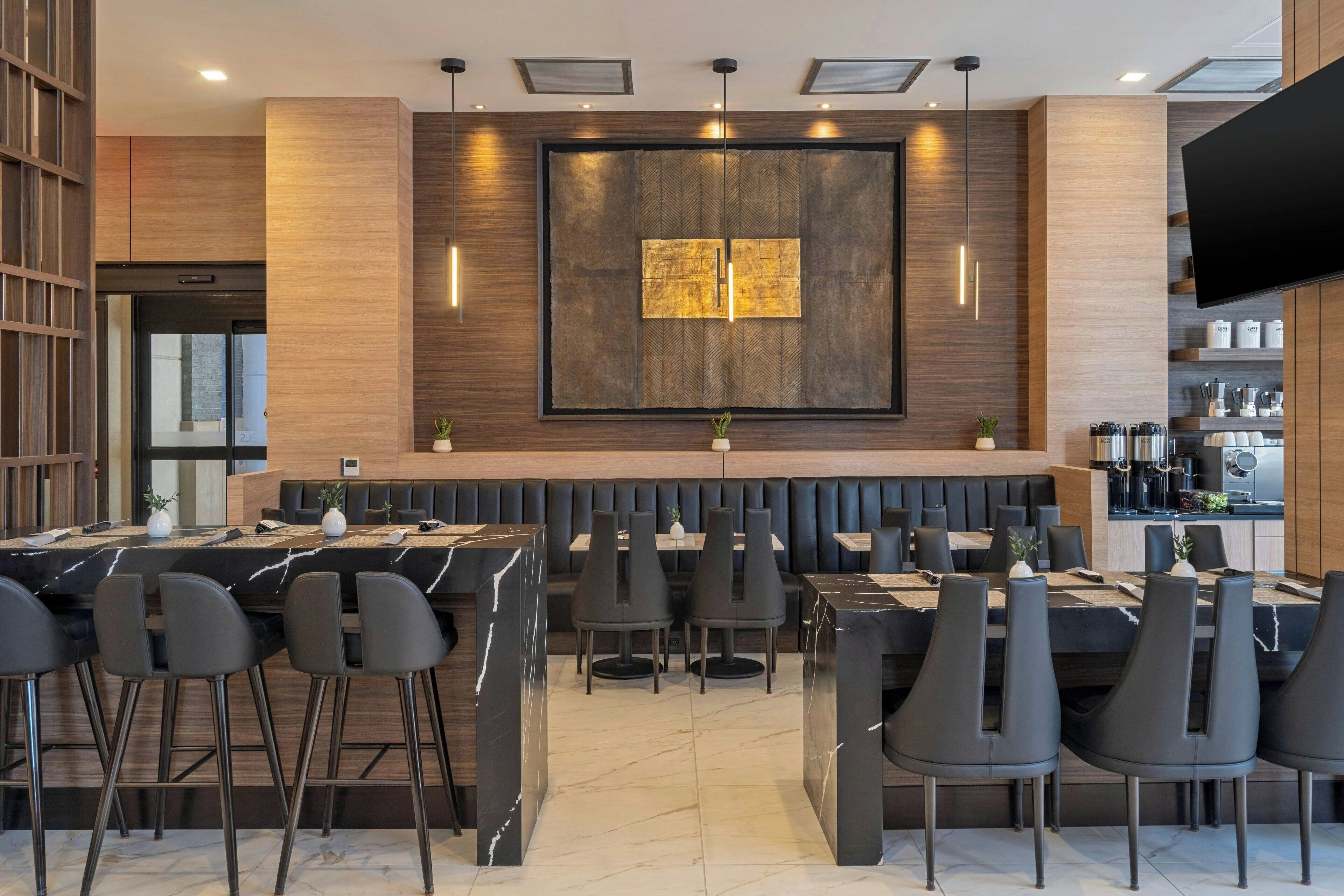 A modern restaurant with a bar area, high stools, and a large wall-mounted TV.
