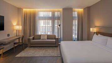 A hotel room with a large bed, a sofa, a desk, and a TV.