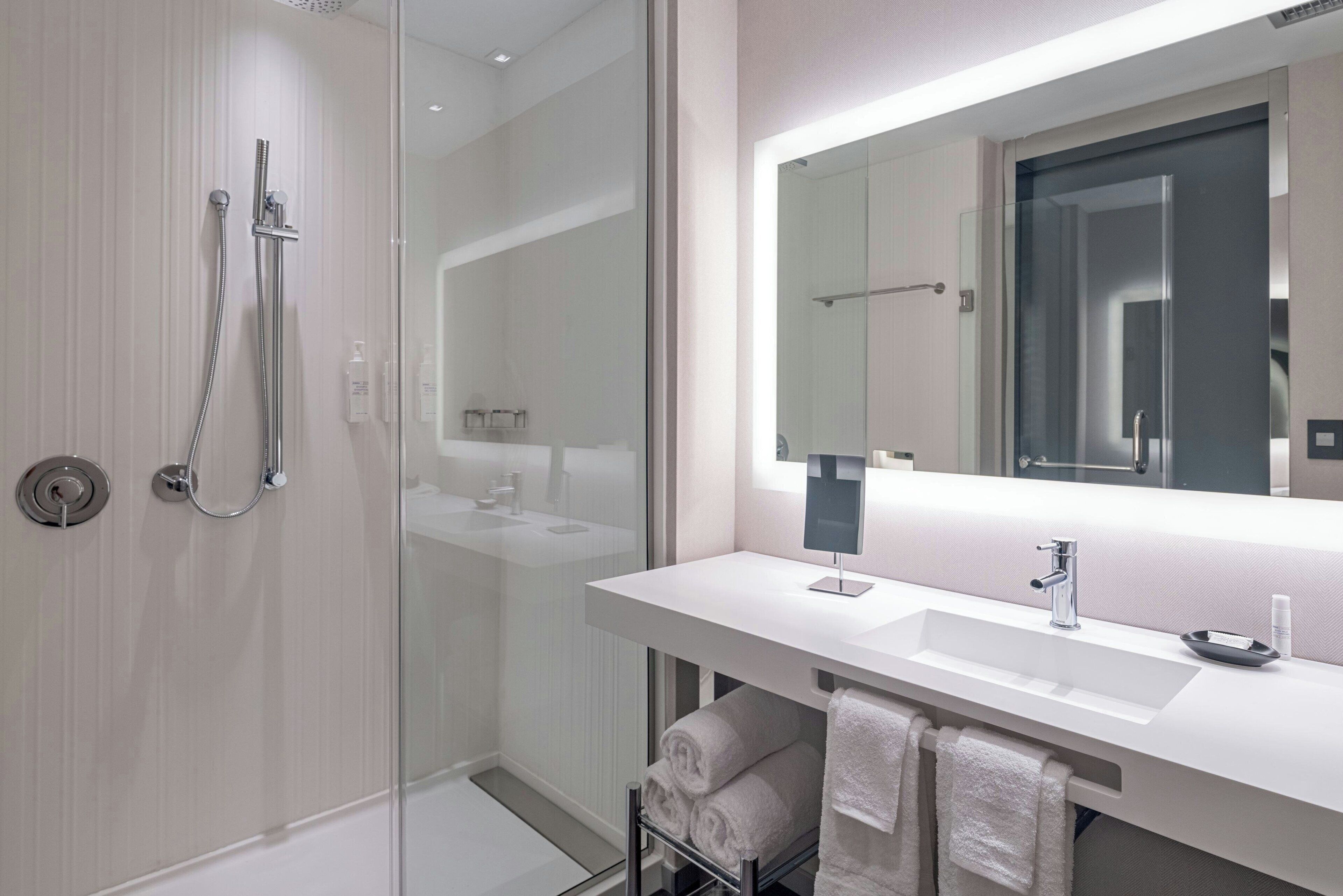 A modern bathroom with a glass-enclosed shower, a large mirror, and a white vanity with a sink.