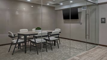 A conference room with a glass partition, a round table with chairs, a small plant, and a mounted TV on the wall.