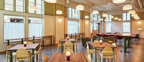 A spacious dining area with multiple tables and chairs, large windows, and hanging pendant lights.