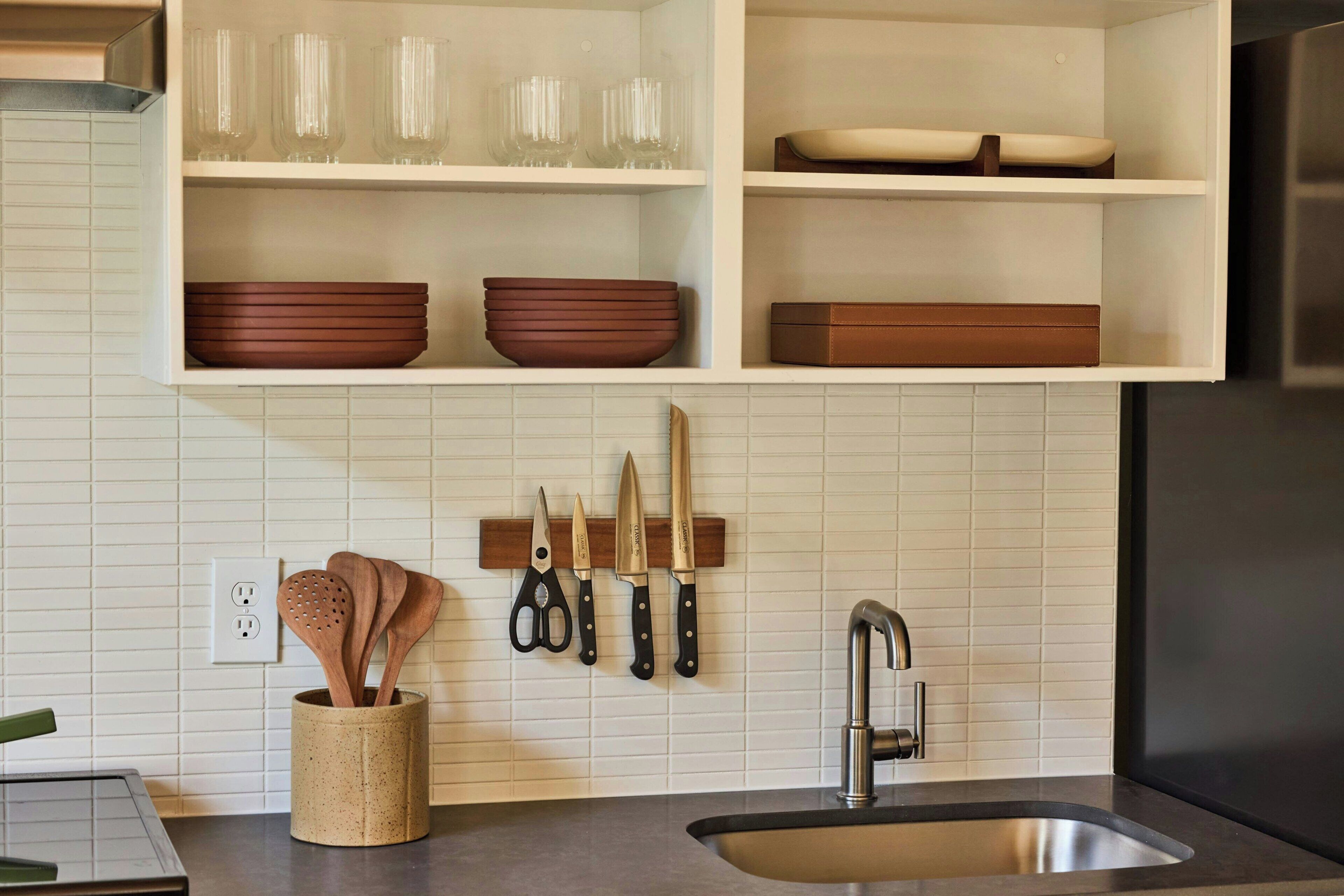 Een keuken met een witte betegelde spatwand, een roestvrijstalen spoelbak en houten keukengerei dat aan de muur hangt.