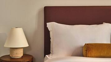 A neatly made bed with white and brown bedding, a round wooden nightstand with a lamp, and two framed abstract art pieces on the wall.