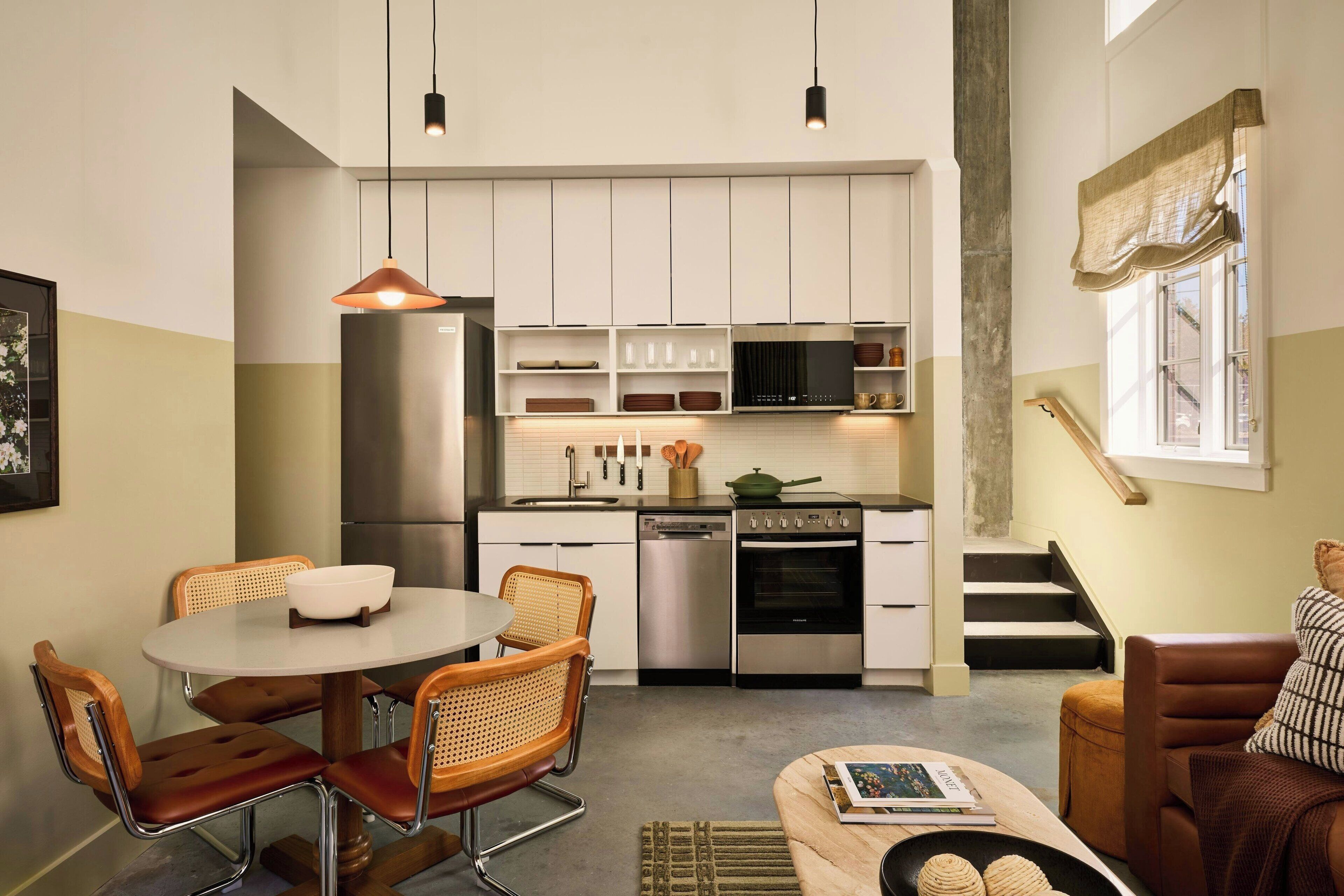 A compact kitchen with white cabinets, stainless steel appliances, and a dining area with a round table and wicker chairs.