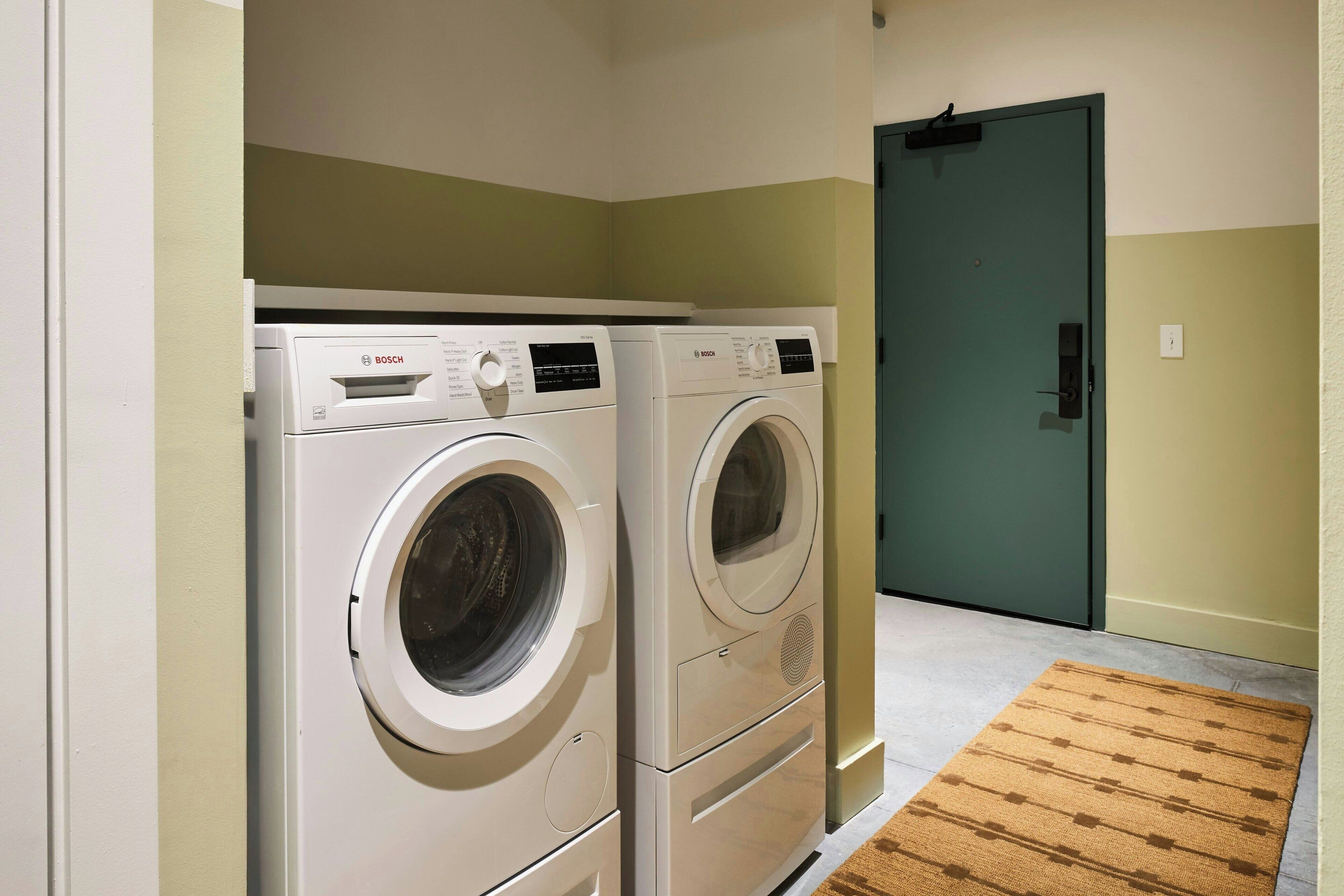 A laundry room with two Bosch washing machines and a green door.
